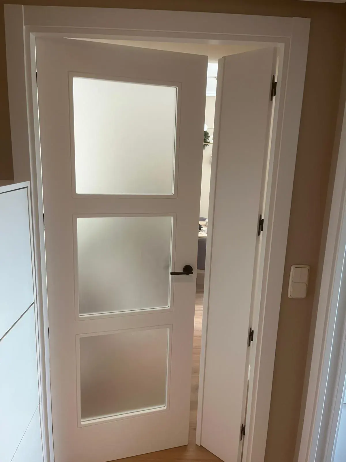 Puerta lacada en blanco con tres cristaleras, abierta en un pasillo
